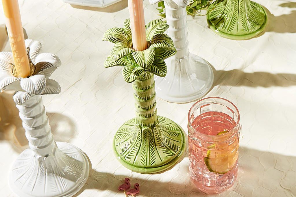 light green palm tree taper candle holders staged on a dinner table with pink drinks 