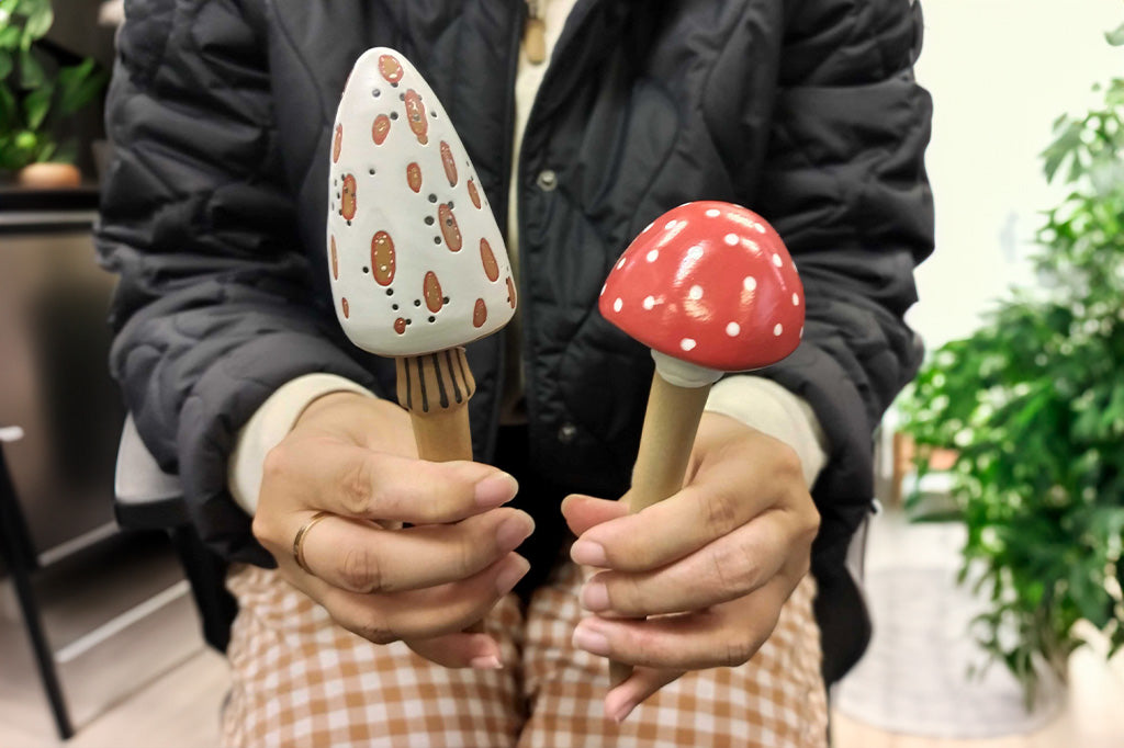 hands holding the pair of red and white mushroom planter stakes 