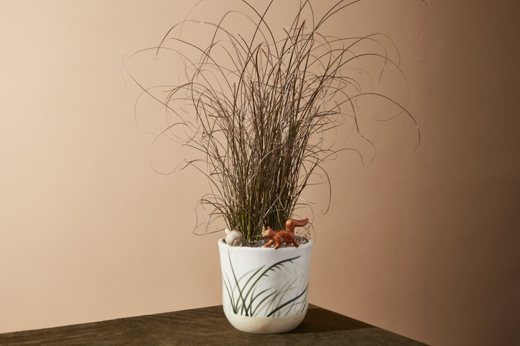 ceramic pot with sculpted squirrel and nut on the rim -shown with bushy ornamental grass