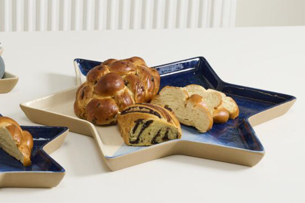 Star of David-shaped ceramic dish with a blue and beige gradient on a white background holding babka and challah