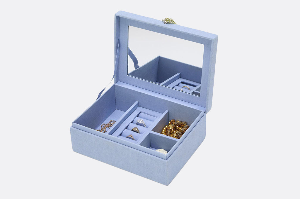 Pale blue embroidered and beaded jewelry box opened to show the mirror interior with example jewelry items in tucking spots