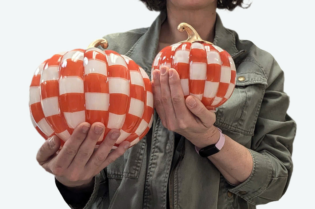 Person holding two checkered pumpkins against a white background