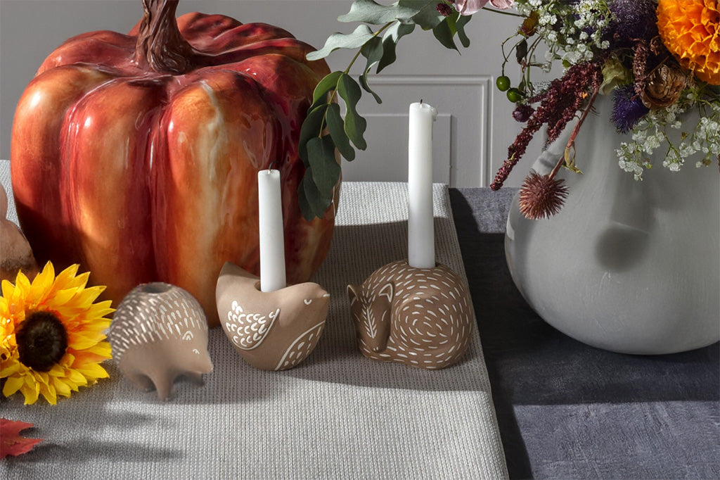 Decorative items including a ceramic pumpkin, candleholders, and flowers on a harvest theme table.