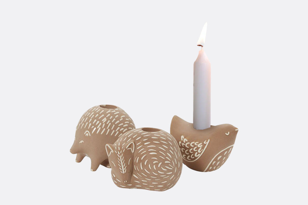 Ceramic fox, bird, and hedgehog-shaped candle holder with a lit candle on a white background