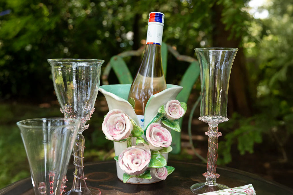 ceramic vase with 3-d sculptured pink roses on front with aqua blue interior cream exterior. holding a chilled bottle of wine 
