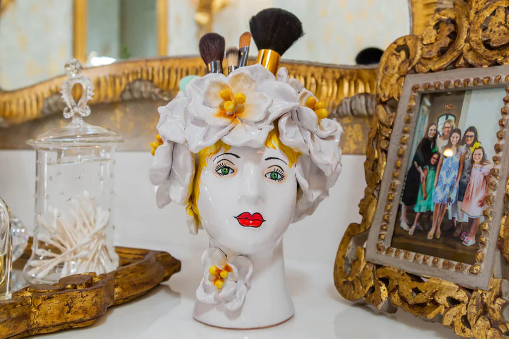 ceramic women's head adorned with big white flowers vase filled with makeup brushes