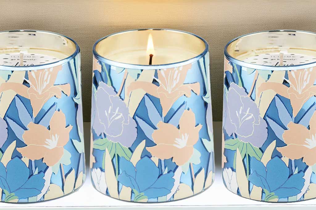 Three floral-patterned candles with a lit candle in the center. glass vessel with metallic rim