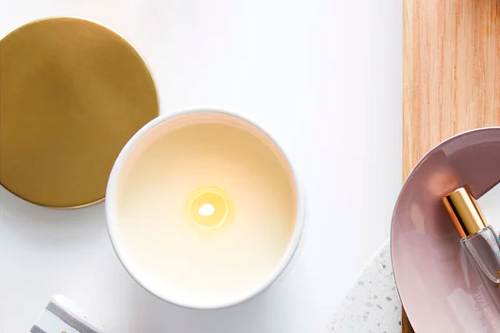Lush Tropics candle shown lit on a vanity table, the gold metal candle lid is set to the side.