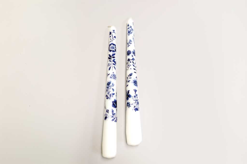 Two white candles with blue floral patterns on a light gray background
