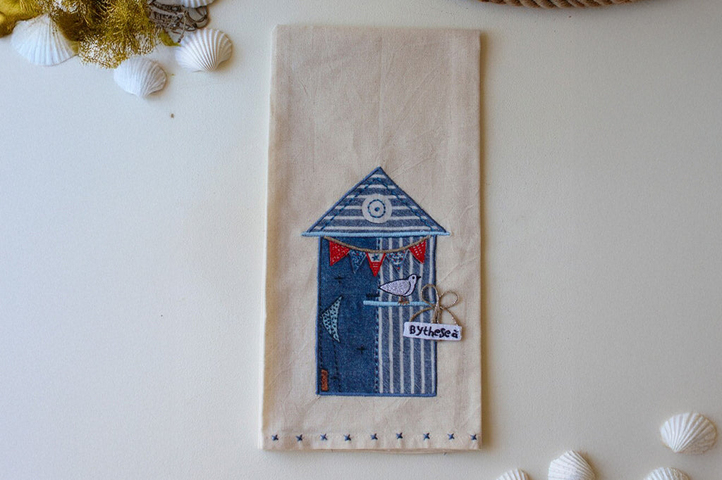 embroidered tea towel of beach house with seagull. embroidered thread in white blue and red 