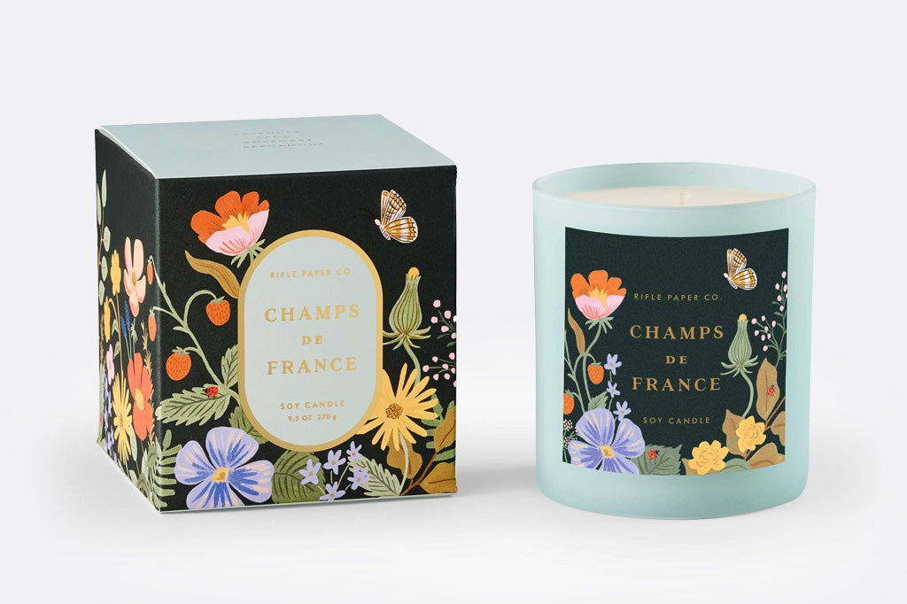 Candle and packaging with floral design in dark teal and light blue with butterflies and blossoms, Champs de France soy candle by Rifle Paper Co.