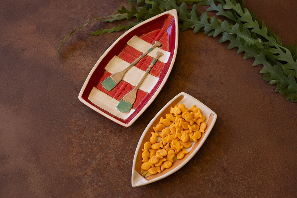 A set of dishes shaped like row boats, one filled with crackers.