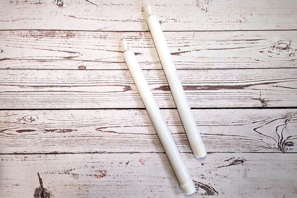 Set of two white LED taper flameless candles laying on wood table