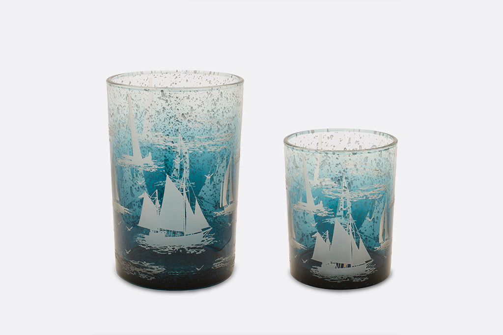 Two candleholders decorated with imagery of sailboats in water.