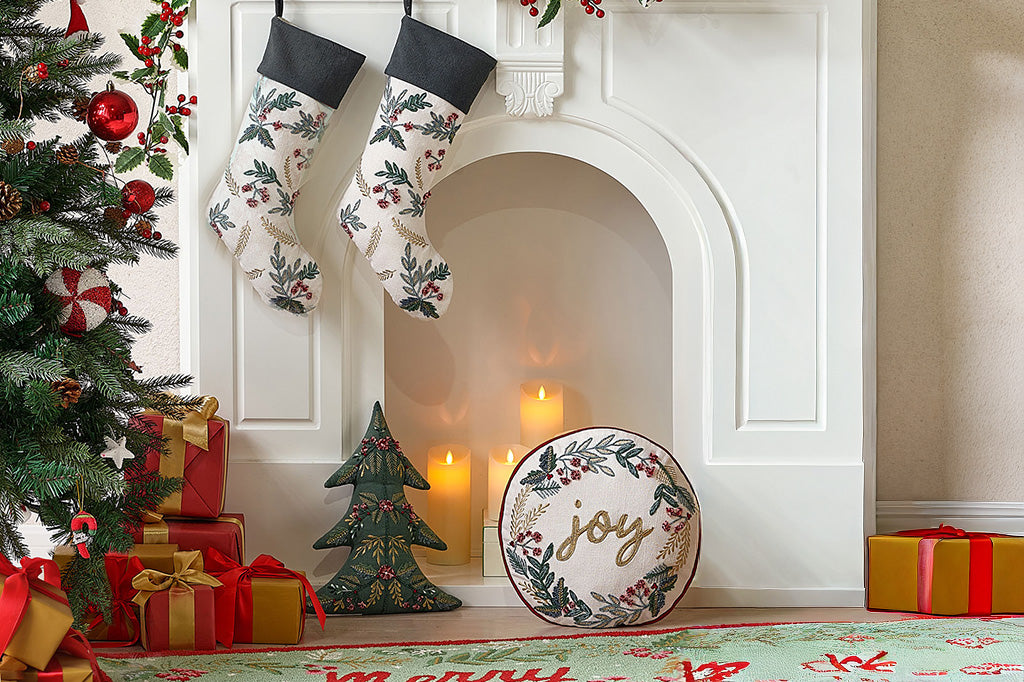 Christmas decor with stockings, tree, presents, and 'joy' pillow in front of a fireplace.