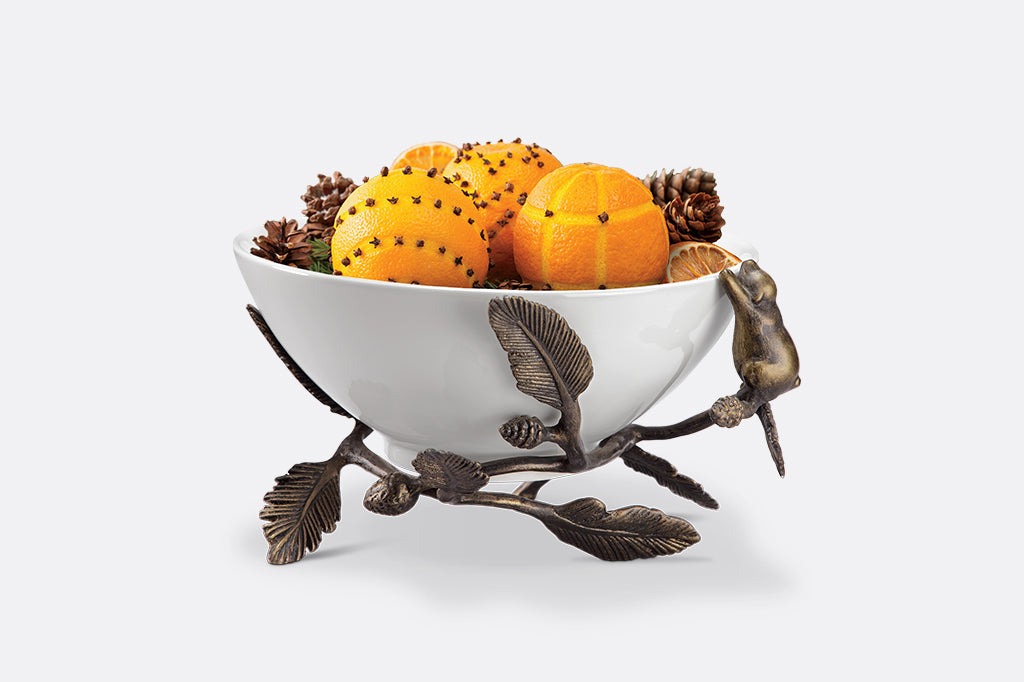 Ceramic bowl holding potpourri clove oranges is nested in cast metal bowl holder featuring bear climbing pine branches