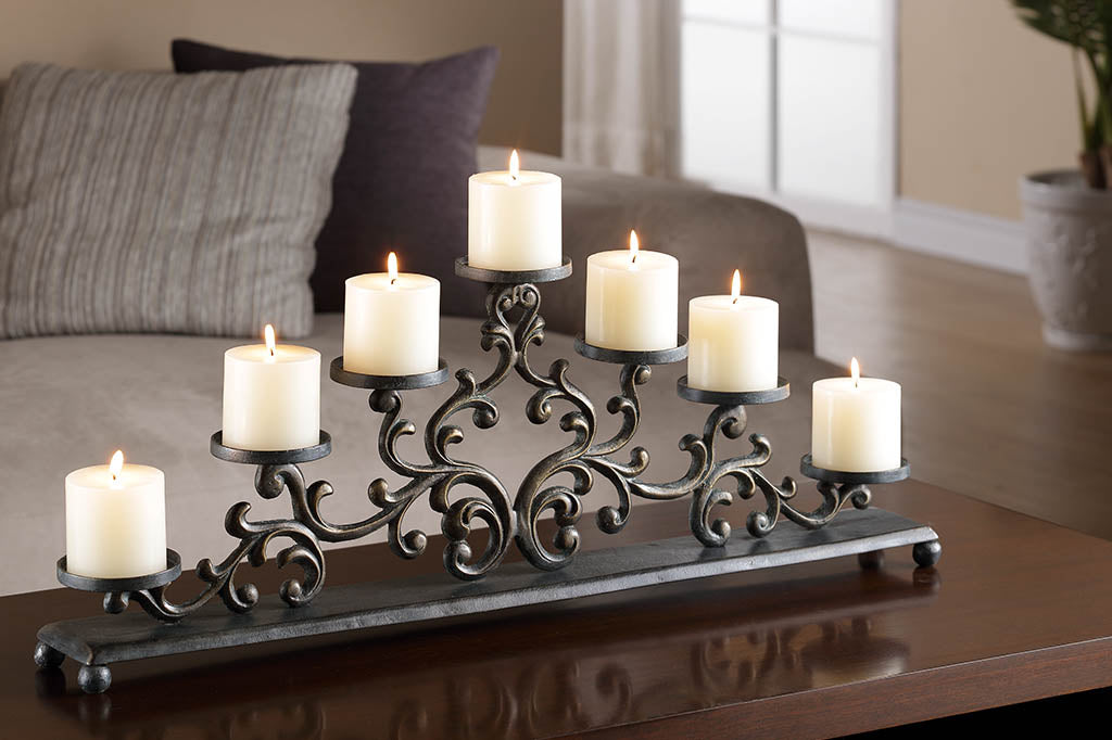 Cast metal candelabra holding 7 pillar candles is comprised of Filagree scrollwork in an elegant triangle, displayed on coffee table by a couch