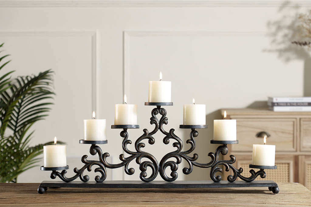 Cast metal candelabra holding 7 pillar candles is comprised of Filagree scrollwork in an elegant triangle, displayed on dining table 