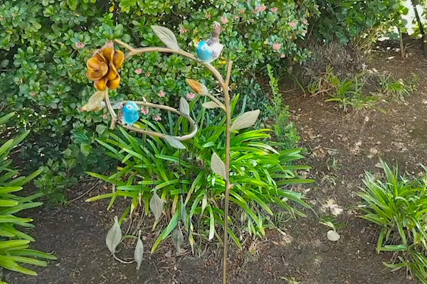 video of wind art moving in the breeze in a flowerbed with shrubs