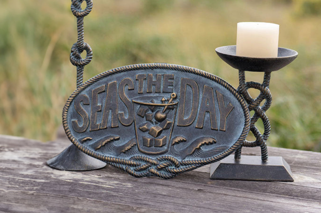 Cast metal wall plaque, reading seas the day with waves and a water glass cup, surrounded by nautical knots