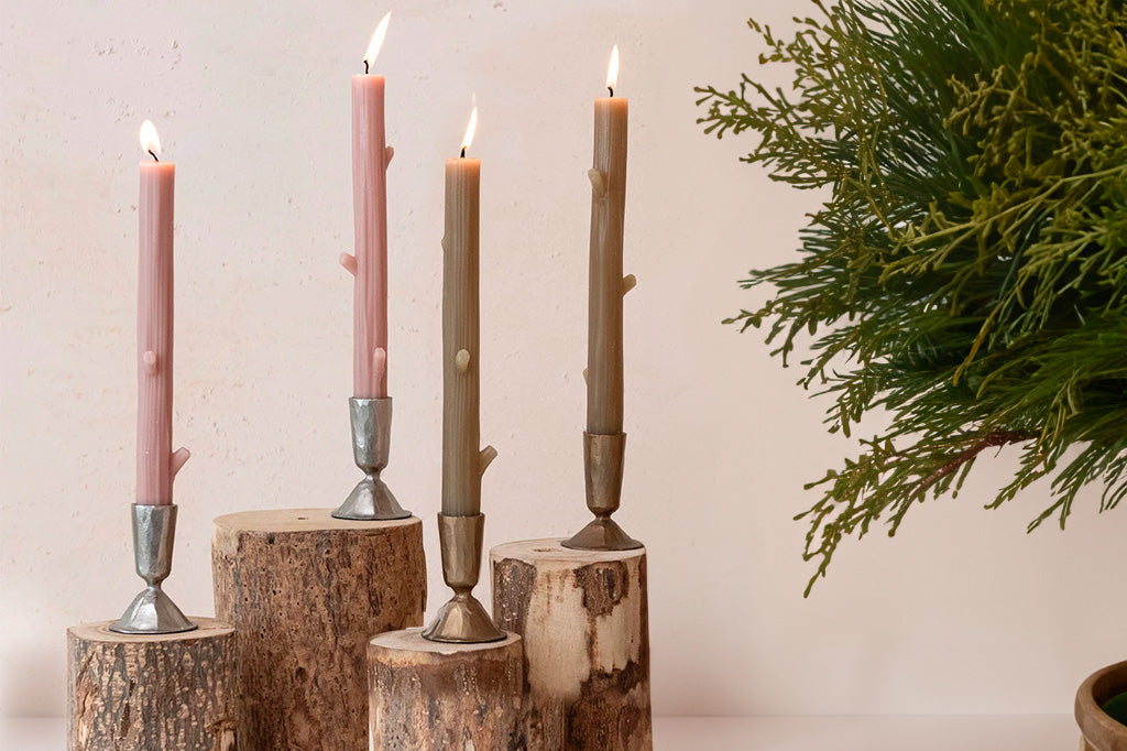 olive colored twig taper candles pack of 4, shown with desert blush in candleholders, propped on wood stumps