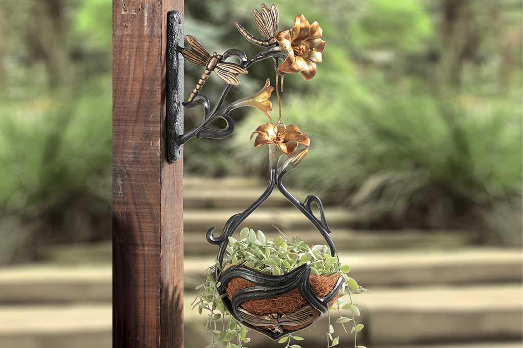 Wall hook and hanging planter with motif of golden lilies and dragonflies mounted to an outdoor post