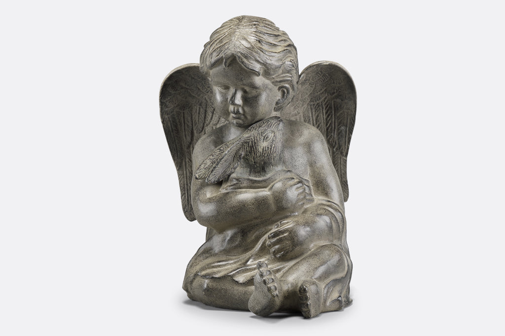 Cast metal cherub with wings holding bunny in blanket face center. Cherub face is slightly downtown and looking left, hugging bunny in lap.