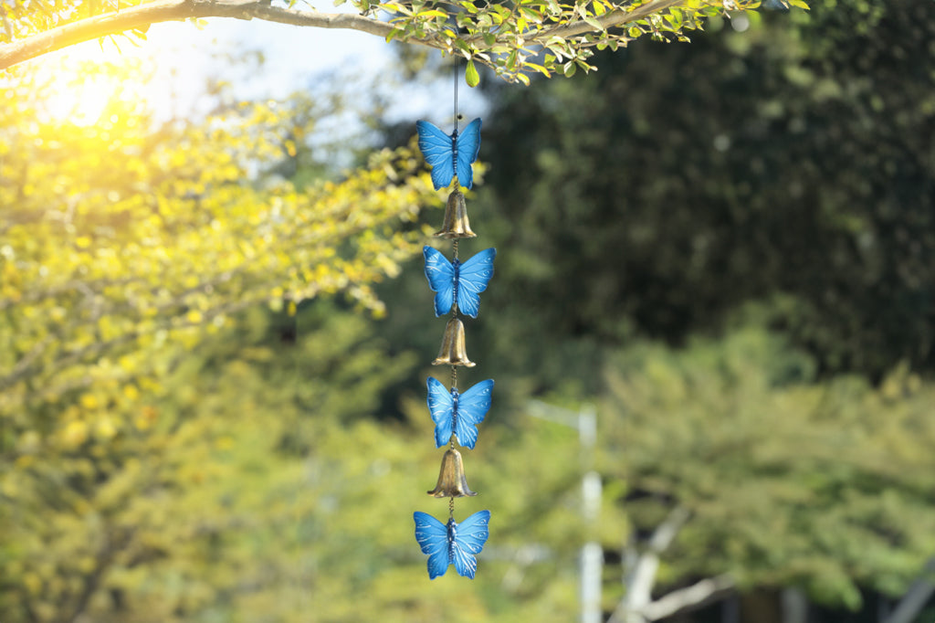 cast metal blue butterfly and bell windchime, hanging from tree in outdoor environment 