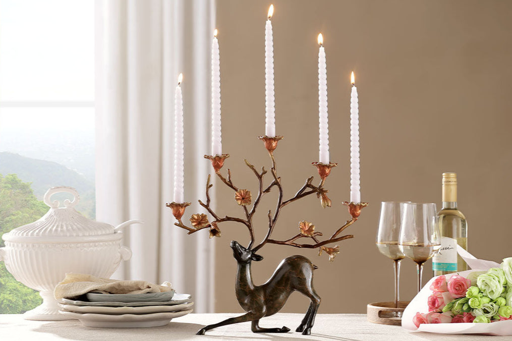 Cast Metal whimsical deer and flora candleholder shows white taper candles amongst blooming antlers on an elegant table set with wine and flowers