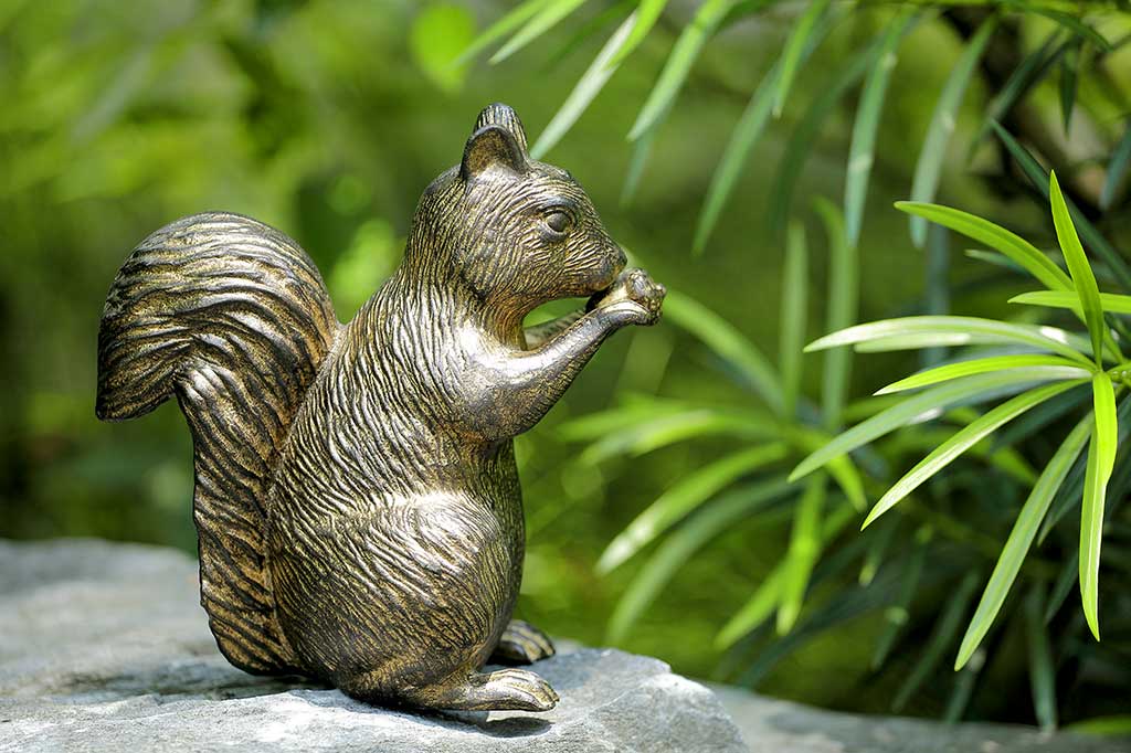 cast metal squirrel statue on a rock with green foliage in the background