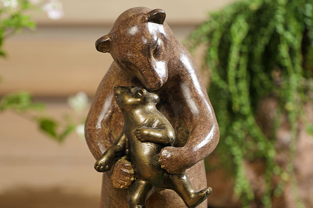 detail closeup of a statue of a bear holding a cub with a blurred green plant background