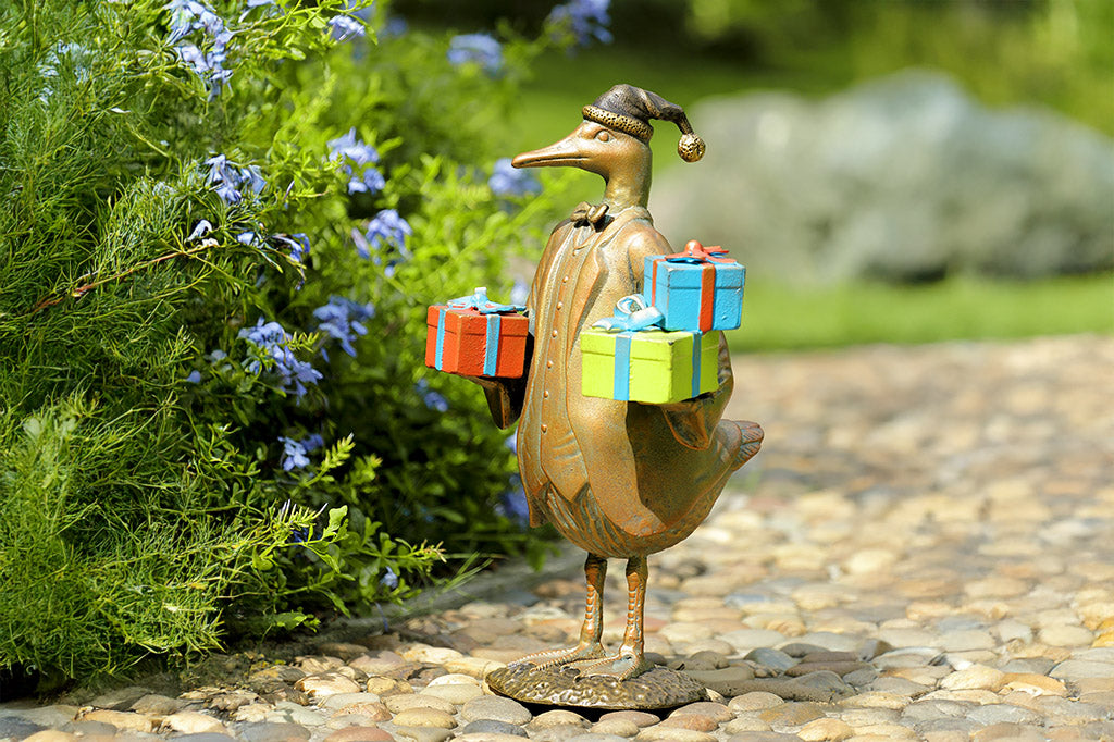 Bronze duck sculpture in formal clothing carrying gift boxes in a garden setting