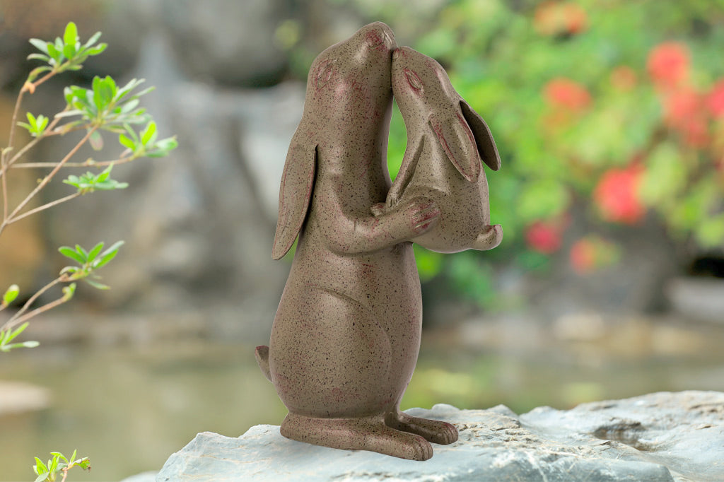 Garden sculpture of rabbit nuzzling a baby bunny in an outdoor setting
