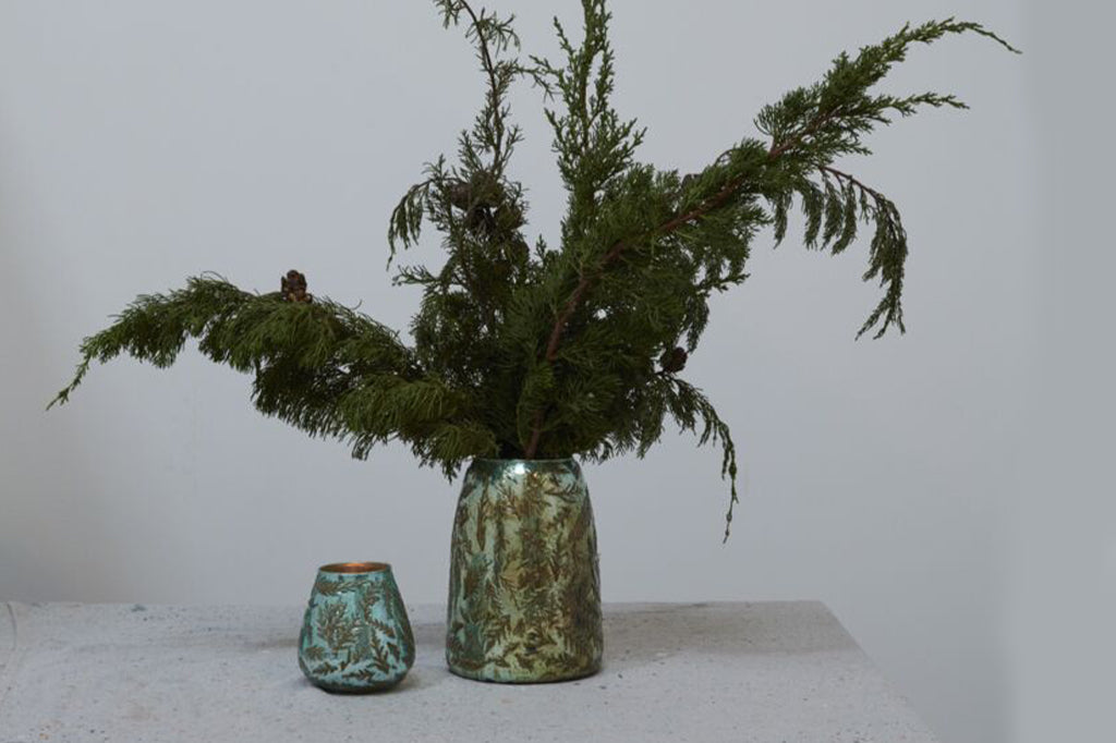 Metallic green vase with juniper texture and design on exterior displayed with juniper branches inside 