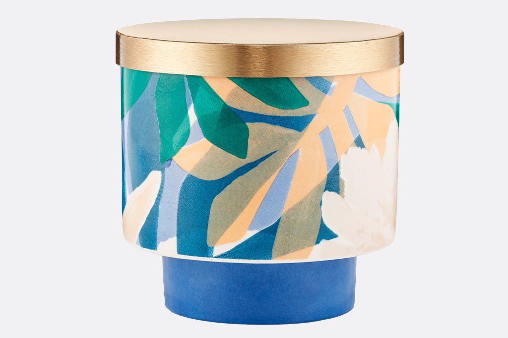 porcelain candleholder with metal lid and candle interior. printed with modern palm-style graphic and lid is gold
