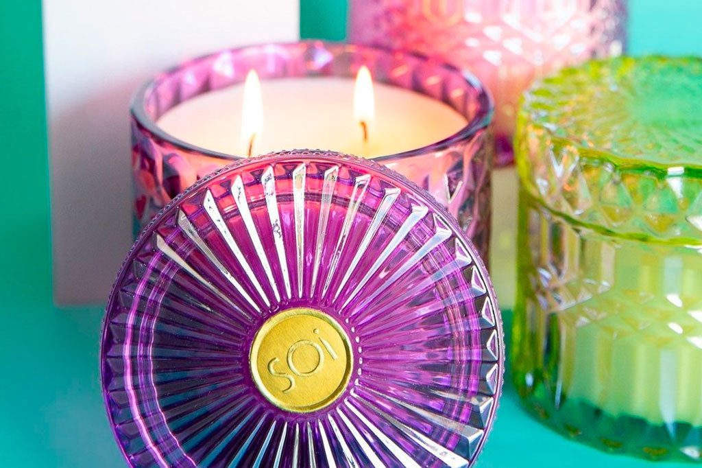 Soy wax floral scented candle in pink, crystal cut-glass vessel with decorative lid shown lit on a green table surrounded by other candle colors and sizes