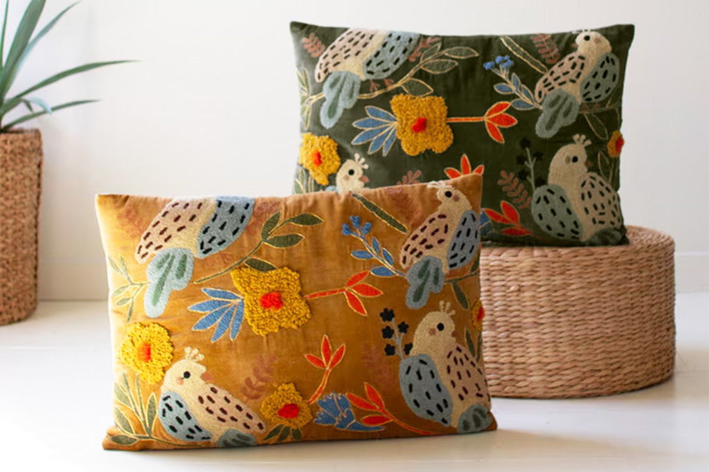 Two embroidered pillows with bird and floral patterns shown on ground near decorative baskets