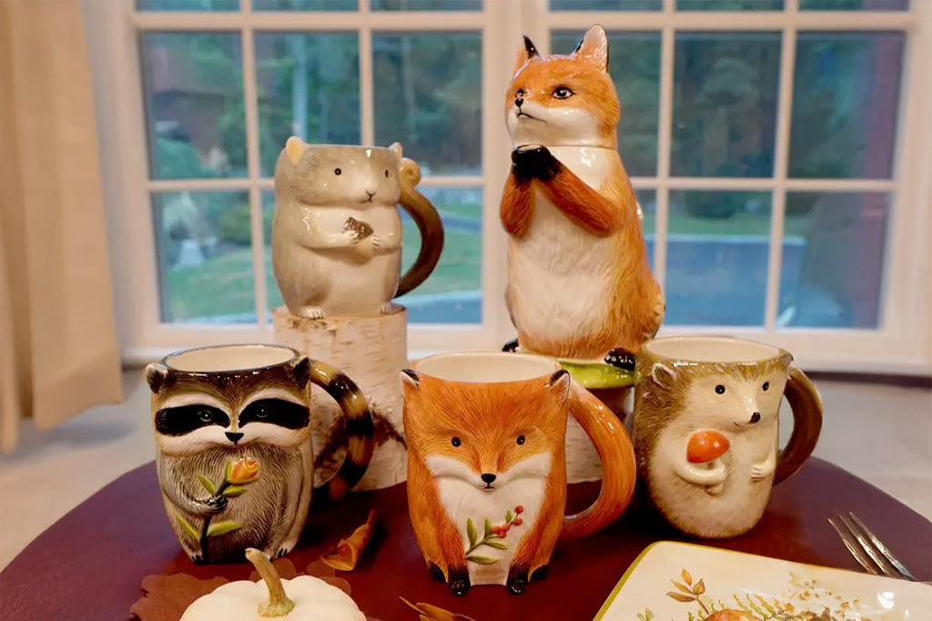Set of animal-themed mugs on a table with a window in the background, coordinating fox-shaped teapot in scene