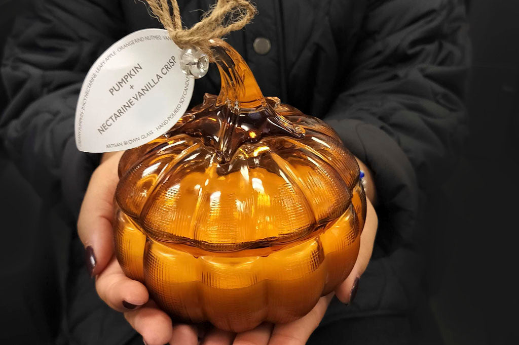 re-usable glass pumpkin candle with scent of pumpkin, vanilla, and nectarine shown in woman's palms