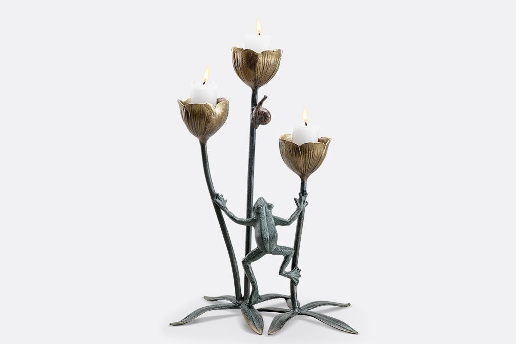 A curious frog watches a snail on a flower stem in a cast metail sculpture and votive candle, holds three candles in the blossoms holder