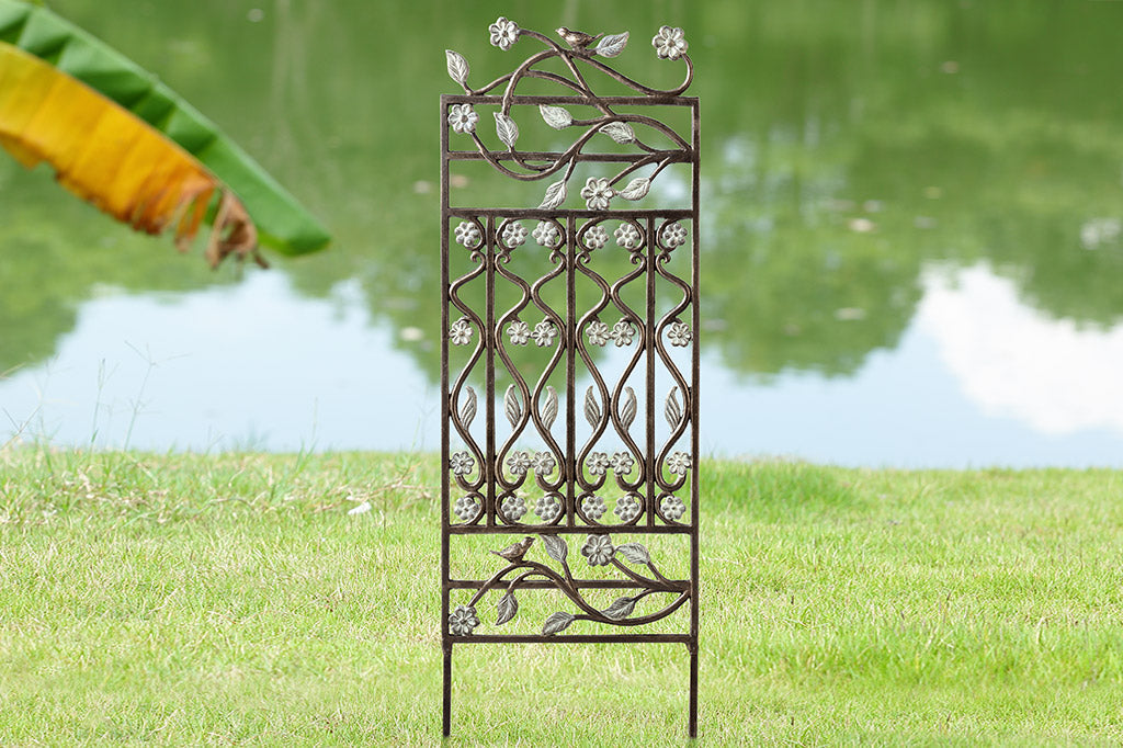 Brindille Trellis features verdi accents, twining branches, and two bird accents. Shown near a lake and banana tree