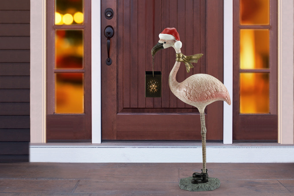 Flamingo holiday sculpture lantern shown with gold scarf and santa hat in red and white. Stagd in front porch of home