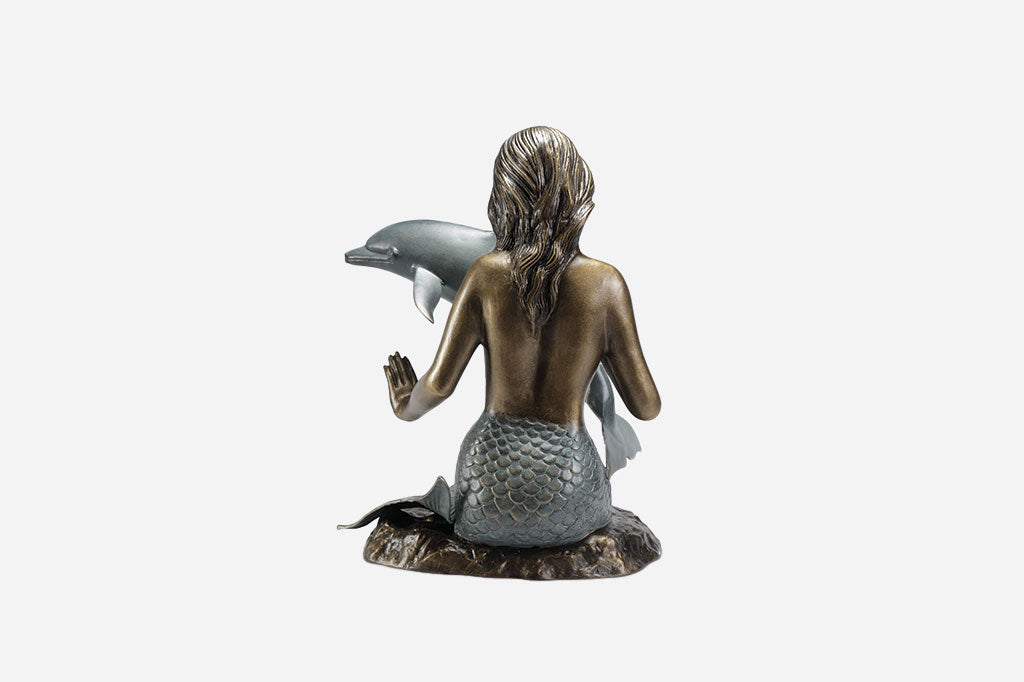 Back view of a mermaid sculpture. Cast metal bronze and verdi mermaid with long hair - she is  reaching out to touch a dolphin