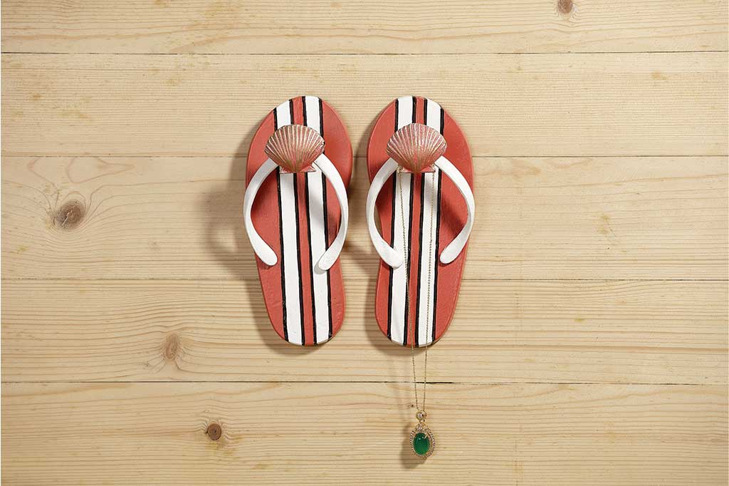 Pair of wall hooks shaped like flipflops holding a necklace on a wood wall