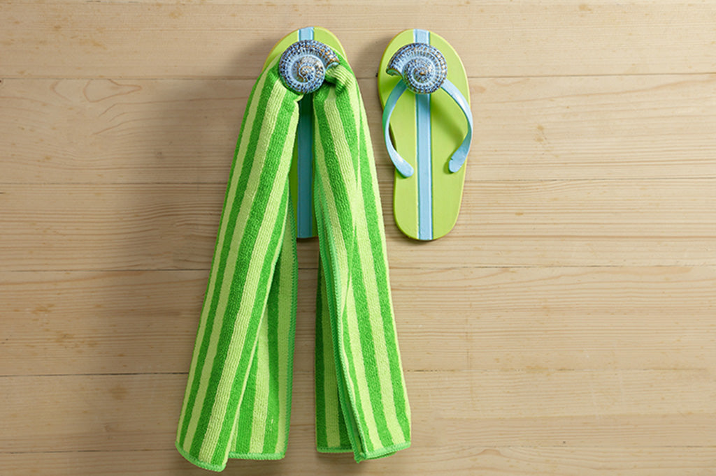 Pair of wall hooks holding a towel on a wood wall. Hooks are shaped like flipflops.