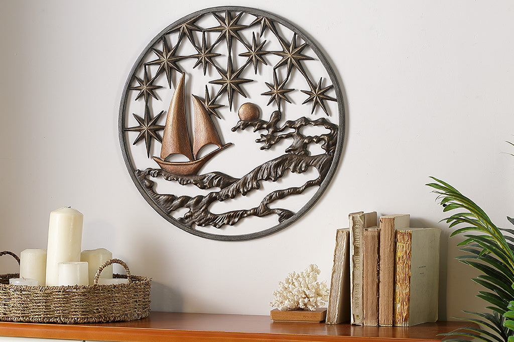 Cast metal circular wall plaque featuring 8-point stars, a moon, sea, and sailboat. It is positioned over a dresser with candles and books.