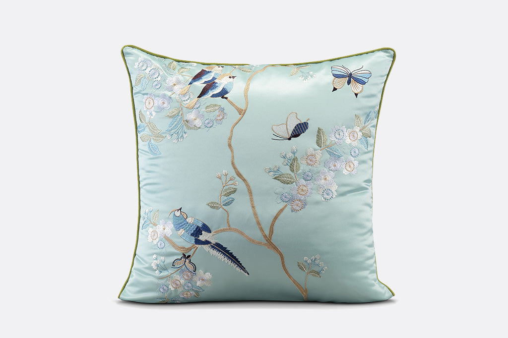 light blue satin pillow with embroidered imagery of birds and butterflies atop flowering branches 