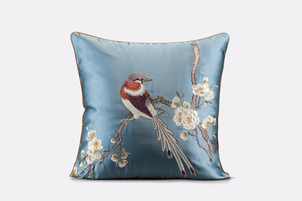 dark blue satin pillow with embroidered details of bird on flowering branch on gray background  