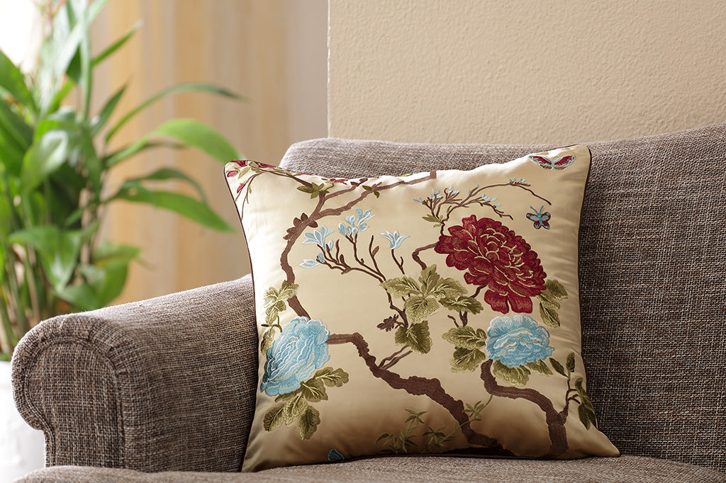 gold satin pillow with embroidered imagery of red and blue flowers with small butterflies and branches set on couch 