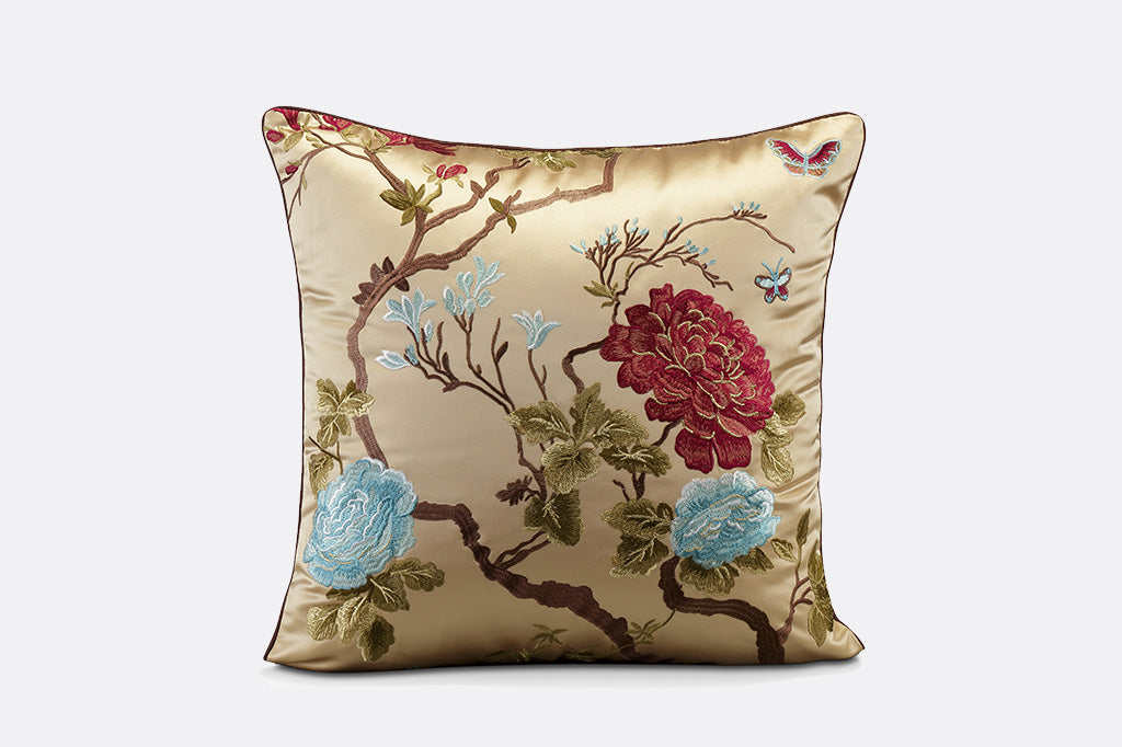 gold satin pillow with embroidered imagery of red and blue flowers with small butterflies and branches  